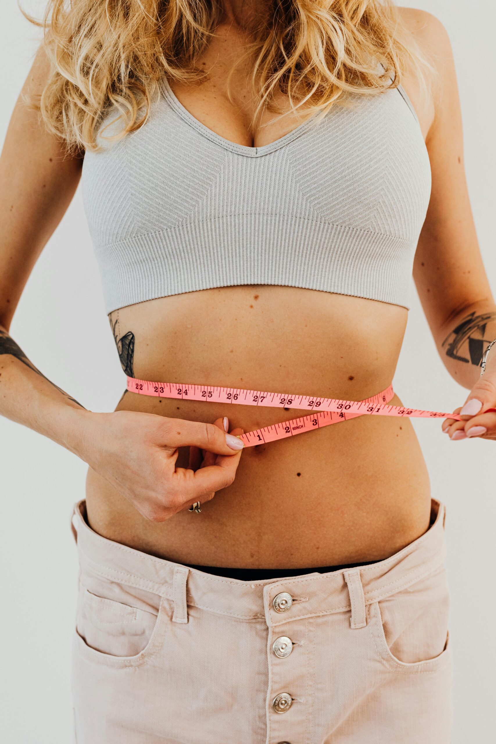 Close-up of a woman measuring her waistline with a tape measure for fitness progress.